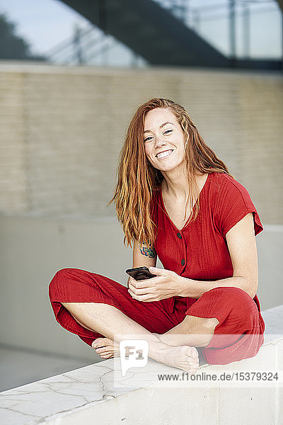 Portrait of smiling sporty young woman having a break using smartphone outdoors