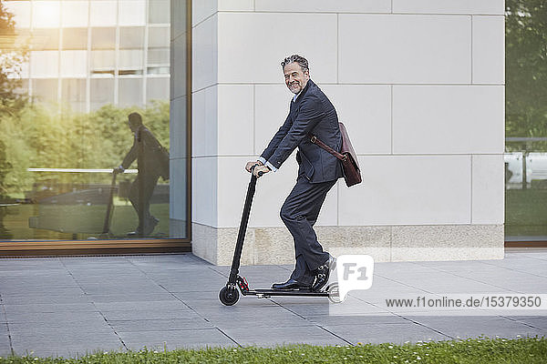 Businessman on e-scooter passing office building in the city