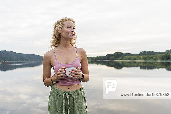 Junge Frau trinkt Kaffee aus Tasse an einem See