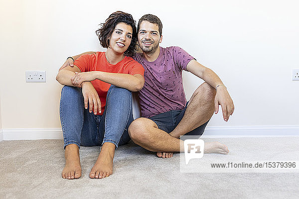 Porträt eines glücklichen Paares auf dem Boden sitzend in neuer Wohnung