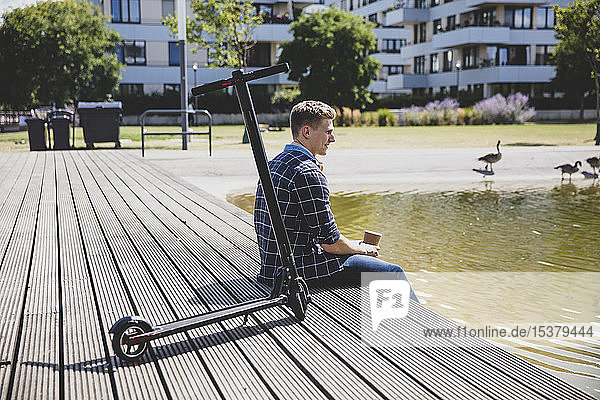 Junger Mann mit E-Scooter sitzt auf der Promenade