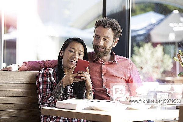 Happy man and woman with cell phone and earbuds in a cafe
