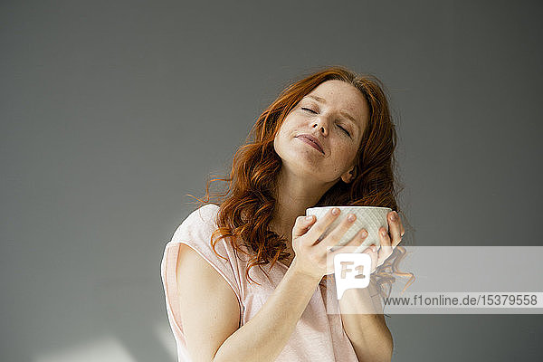 Bildnis einer entspannten rothaarigen Frau mit Müslischale vor grauem Hintergrund