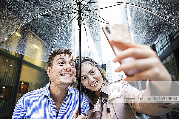 Glückliches Paar mit Regenschirm beim Selfie in Ginza  Tokio  Japan