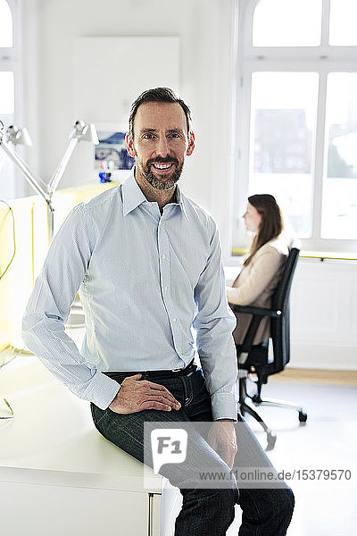 Portrait of smiling businessman in office with employee in background