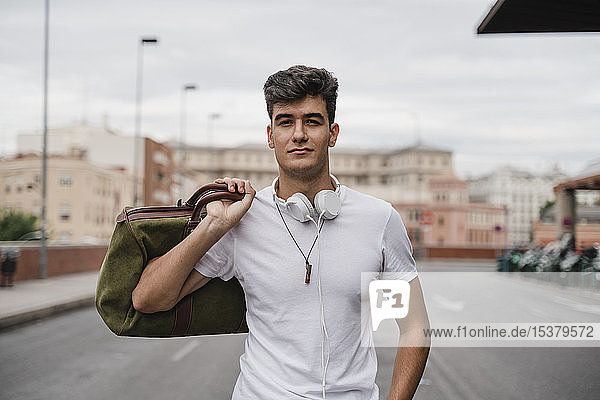 Junger Mann mit einer Tasche am Bahnhof mit Kopfhörern