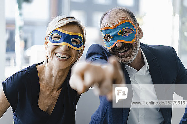 Geschäftsmann und -frau mit Superhelden-Masken  die auf die Kamera zeigen