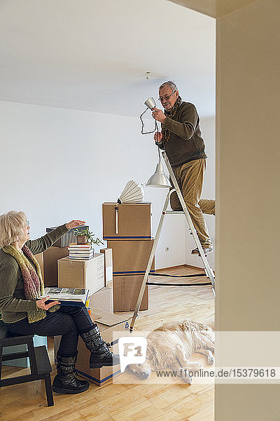 Älteres Ehepaar in einem neuen Zuhause mit einer Deckenleuchte zur Montage durch einen Mann
