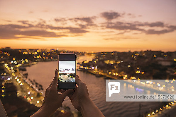 Frauenhände halten ein Smartphone mit einem Foto mit Panoramablick auf Porto bei Sonnenuntergang  Portugal