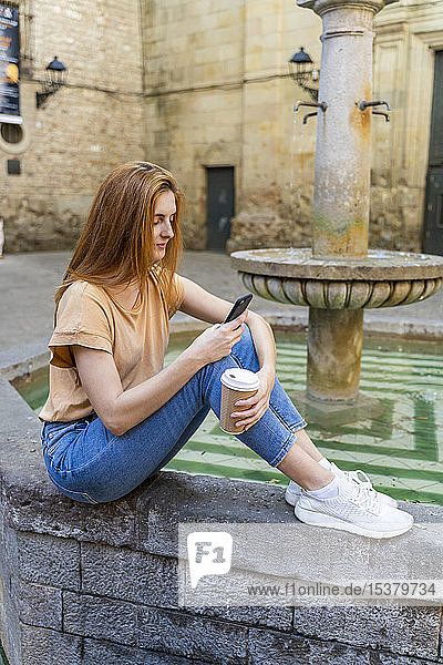 Frau mit Smartphone auf einem Brunnen sitzend
