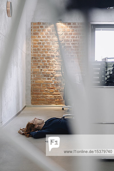 Müde Geschäftsfrau liegt im Büro auf dem Boden