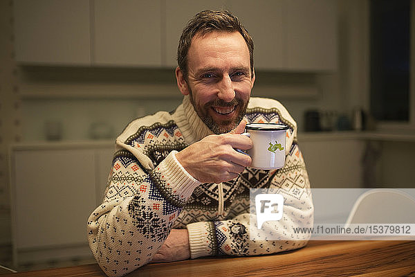 Portrait of happy casual businessman with mug sitting at table at home