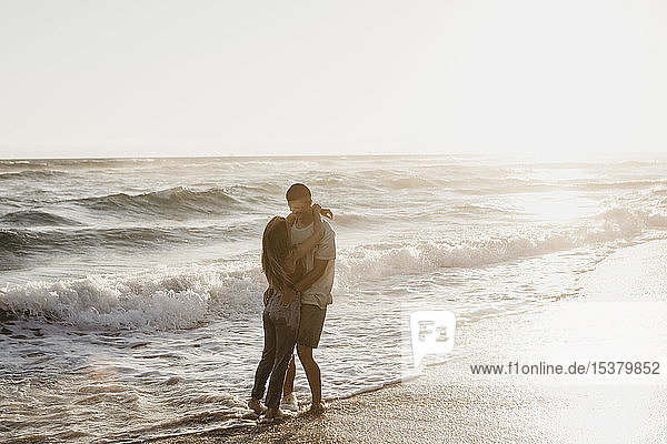 Liebenswertes junges Paar umarmt sich bei Sonnenuntergang am Meeresufer