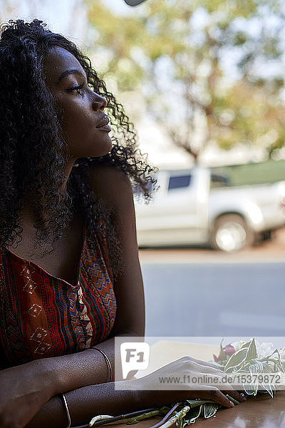 Portrait of young African woman with flowers on the table in a cafe  looking out of window