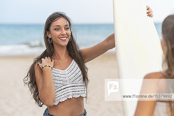 Portrait of smiling young woman with surfboard looking at friend on the beach