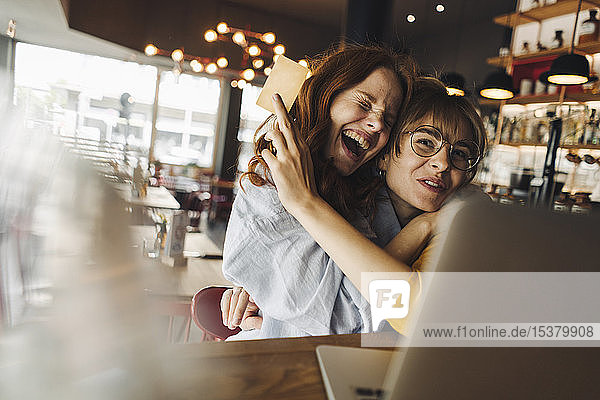 Zwei aufgeregte Freundinnen mit Laptop und Kreditkarte in einem Cafe