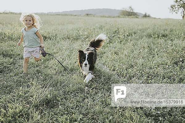 Mädchen rennt mit Hund auf einer Wiese auf dem Land