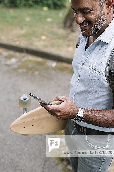 Glücklicher Gelegenheits-Geschäftsmann mit Skateboard und Smartphone in der Stadt