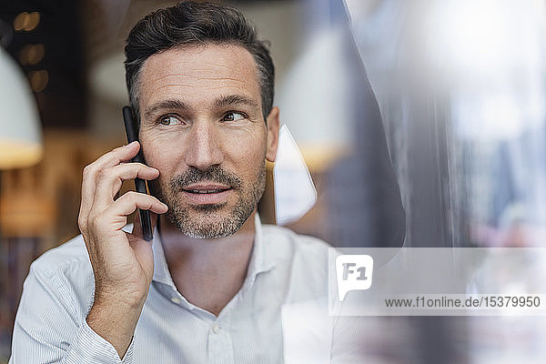Porträt eines Geschäftsmannes am Telefon hinter einer Fensterscheibe in einem Cafe