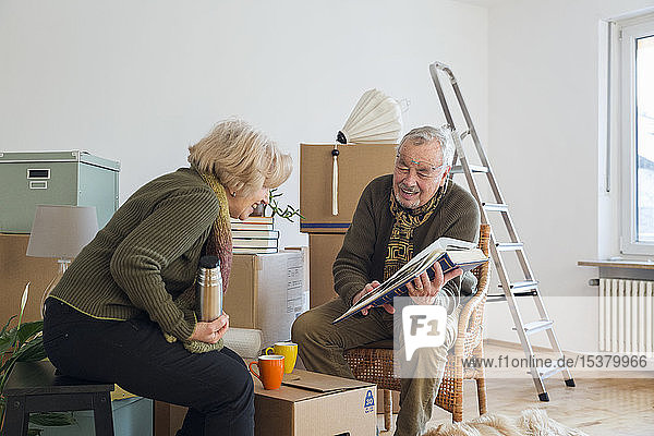 Älteres Ehepaar betrachtet Fotoalbum umgeben von Pappkartons in einem leeren Raum