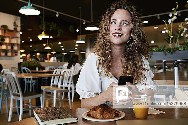Smiling young woman with smartphone in a cafe having breakfast