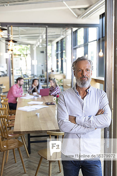 Porträt eines reifen Geschäftsmannes in einem Cafe mit Kollegen  die im Hintergrund eine Besprechung abhalten