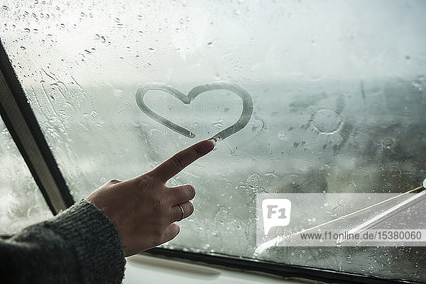 Woman's finger drawing a heart on the window of a van