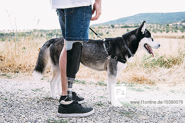 Junger Mann mit Beinprothese mit Hund auf Feldweg