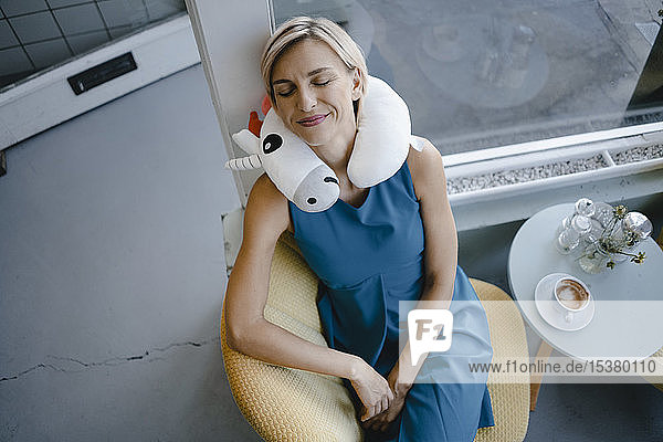 Lächelnde Frau sitzt auf einem Stuhl  macht ein Nickerchen mit einem Einhornkissen um den Hals