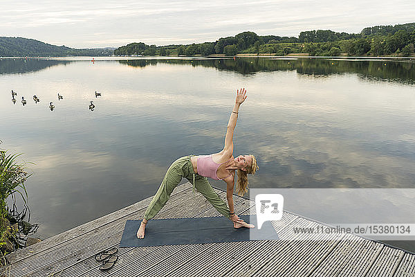 Young woman doing gymnastics on a jetty at a lake
