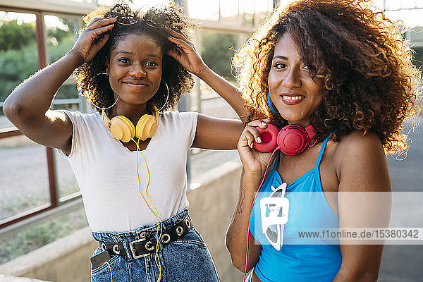 Portrait of two happy young women with headphones at evening twilight