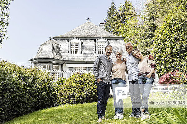 Happy senior couple with adult children standing in garden of their home