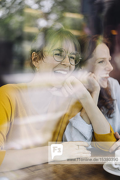 Zwei glückliche Freundinnen hinter einer Fensterscheibe in einem Cafe