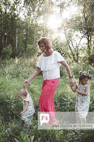 Mutter mit zwei Töchtern  die auf einer Wiese spazieren gehen