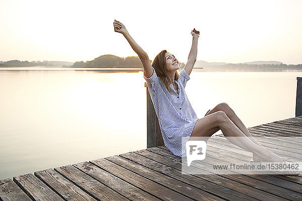 Glückliche reife Frau sitzt bei Sonnenaufgang auf einem Steg an einem See