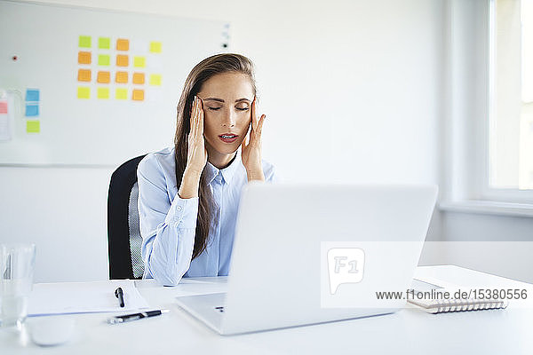 Young businesswoman sitting in office suffering from headache