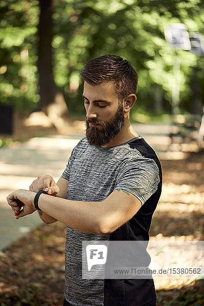 Sportlicher Mann im Wald bei der Kontrolle seiner Smartwatch