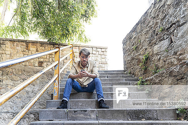 Man sitting on outdoor stairs using cell phone