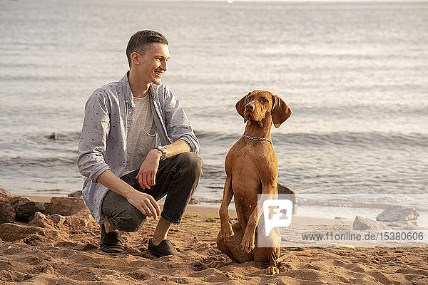 Junger Mann mit seinem Hund beim Training am Strand