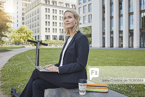 Businesswoman sitting on a wall in the city using laptop
