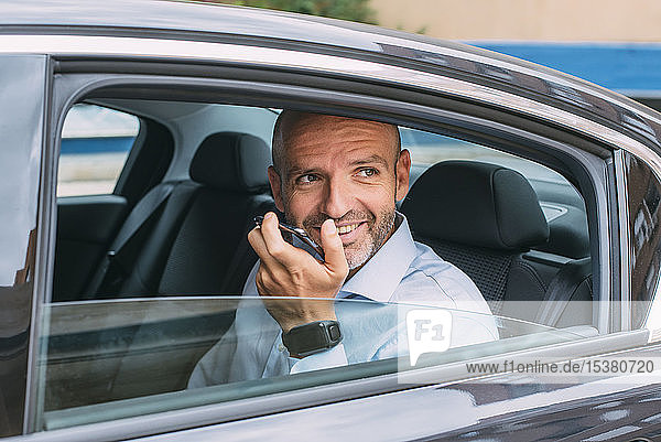 Businessman sitting on a backseat of a car using smartphone and looking around
