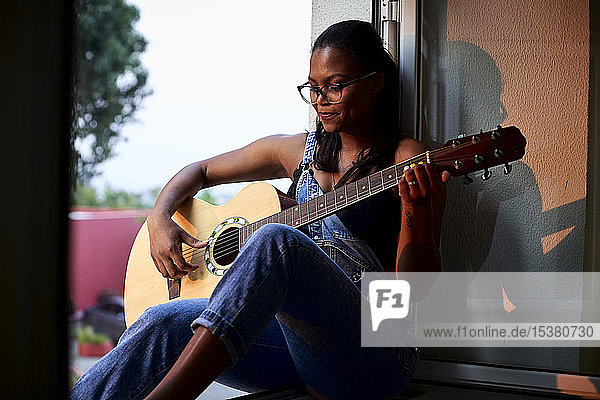 Am Fensterrand sitzende  Gitarre spielende Frau