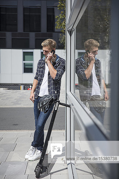 Junger Mann mit E-Scooter telefoniert in der Stadt