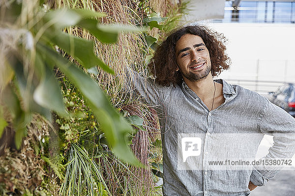 Portrait of smiling young man in front of plant wall