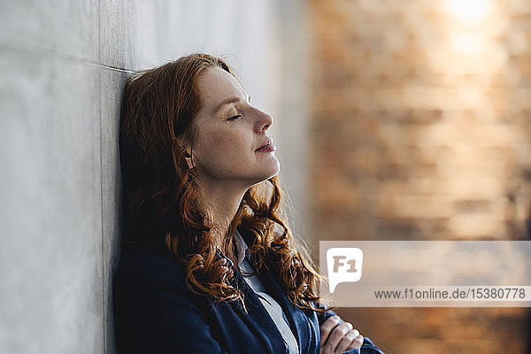 Redheaded businesswoman having a break leaning against a wall in office