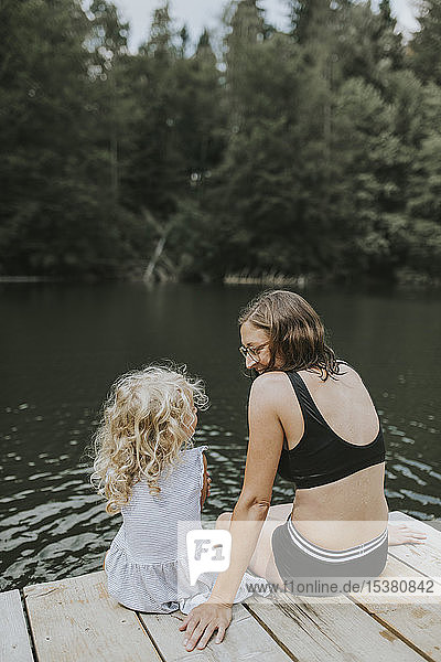 Mother and daughter sitting on jetty at a lake