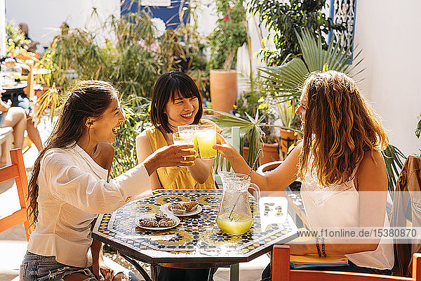 Drei glückliche Freundinnen treffen sich in einem Café mit klirrenden Limonadengläsern