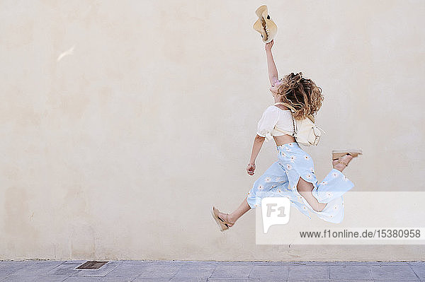 Carefree young woman with hat jumping at a wall