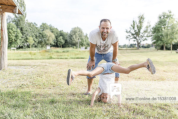 Girl doing headstand on meadow with father standing behind