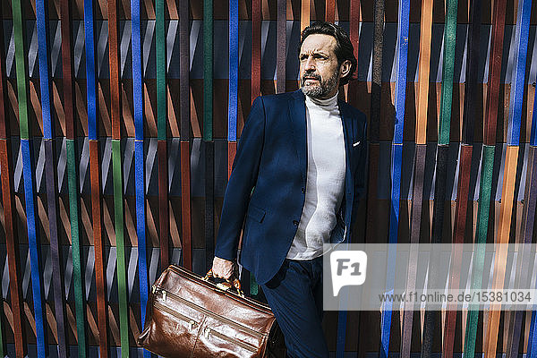 Porträt eines reifen Geschäftsmannes mit Lederaktentasche  der etwas beobachtet